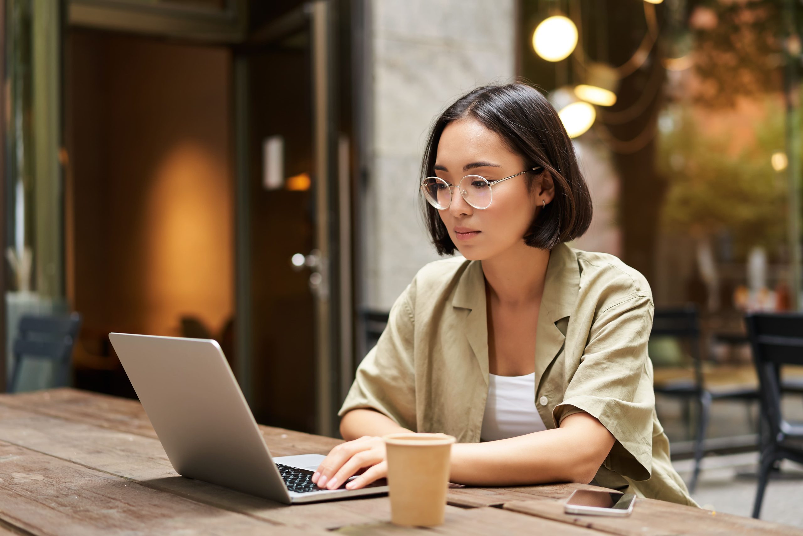 young-woman-working-cafe-using-laptop-drinking-coffee-asian-girl-student-with-computer-stud (1) Freelancer sedang bekerja menggunakan laptop untuk mengelola pekerjaan dan pajak penghasilan